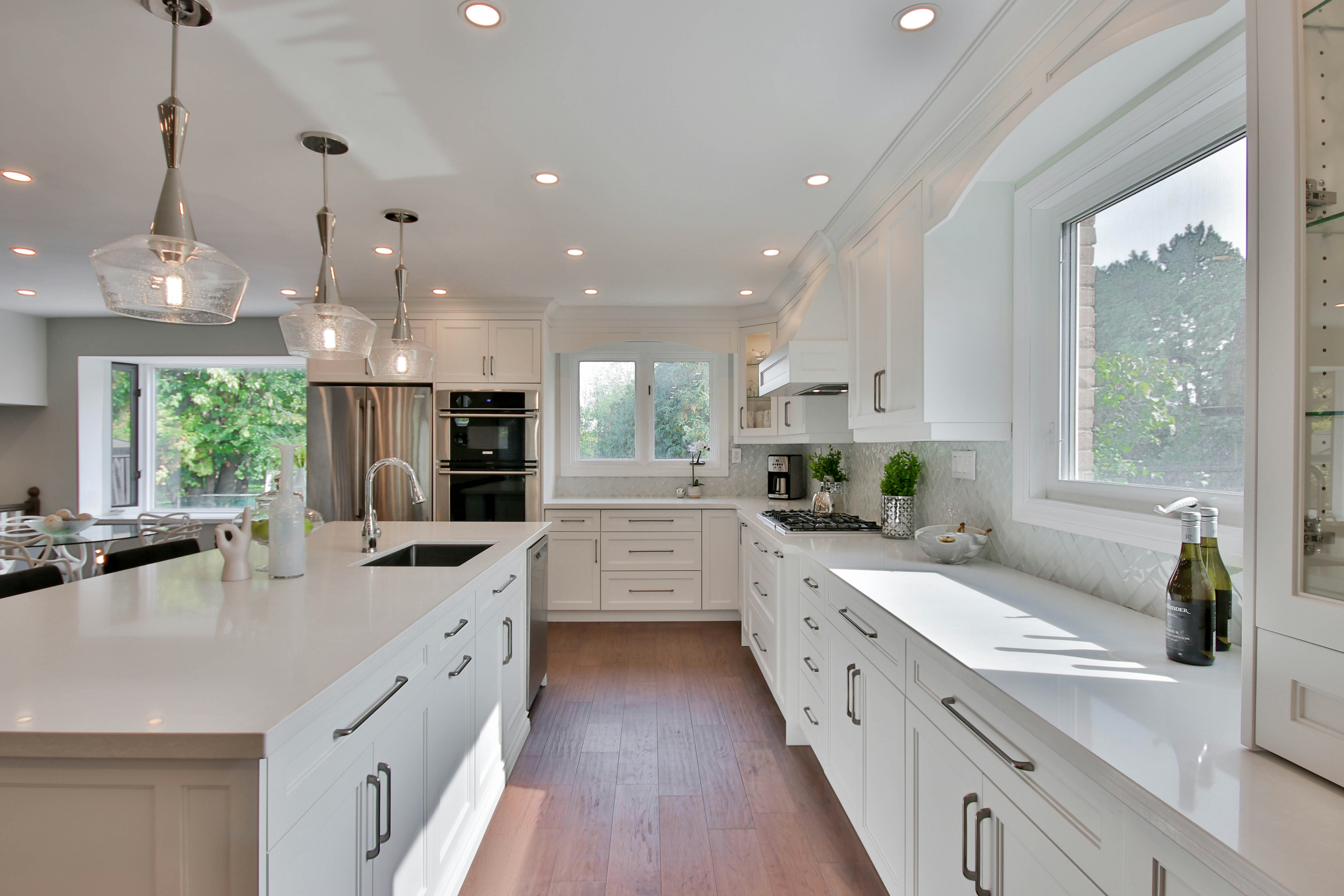 white renovated kitchen with quartz countertops 3 pendant lights over an island with stainless steel appliances